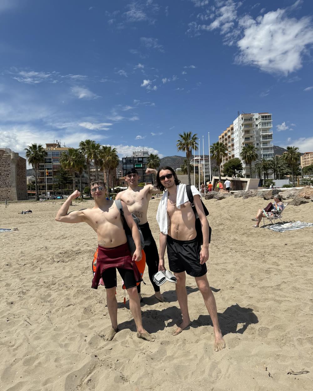 Three swimmers on a sandy beach with palms and apartment blocks behind