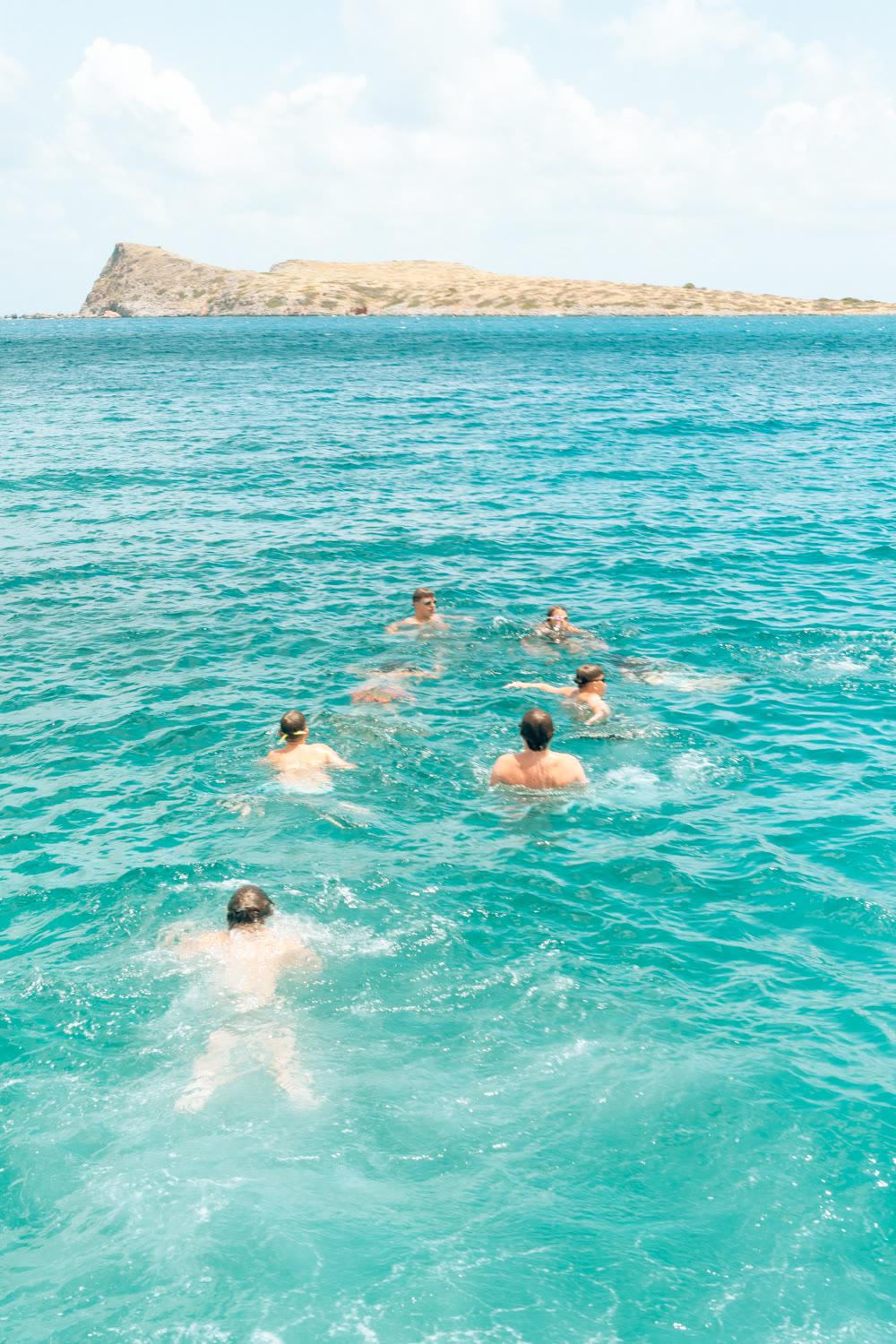 Campers swimming through turquoise water towards a small island